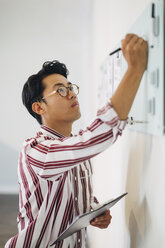 Serious businessman holding clipboard while writing on whiteboard in office - CAVF47718