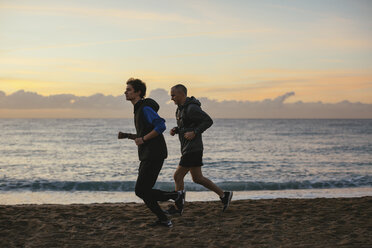 Seitenansicht von Vater und Sohn beim Joggen am Strand gegen den Himmel bei Sonnenuntergang - CAVF47727