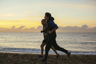 Entschlossener Vater und Sohn joggen am Strand gegen bewölkten Himmel bei Sonnenuntergang - CAVF47729