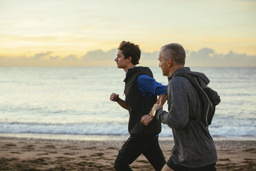 Vater und Sohn joggen am Strand gegen bewölkten Himmel bei Sonnenuntergang - CAVF47730