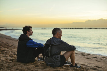 Nachdenklicher Vater und Sohn ruhen sich bei Sonnenuntergang am Strand vor dem Himmel aus - CAVF47731