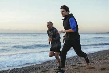 Vater und Sohn joggen zusammen am Strand gegen den Himmel - CAVF47744