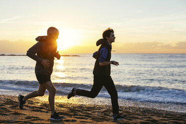 Vater und Sohn joggen am Strand gegen das Meer bei Sonnenuntergang - CAVF47748