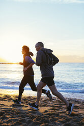 Seitenansicht von Vater und Sohn beim Joggen am Strand gegen das Meer bei Sonnenuntergang - CAVF47749