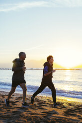 Selbstbewusster Vater und Sohn joggen am Strand gegen den Himmel bei Sonnenuntergang - CAVF47750