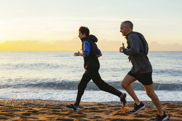 Vater und Sohn joggen in voller Länge am Strand gegen den Himmel bei Sonnenuntergang - CAVF47751