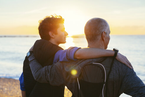 Vater und Sohn legen die Arme um die Schultern und betrachten die Aussicht, während sie am Strand stehen - CAVF47754