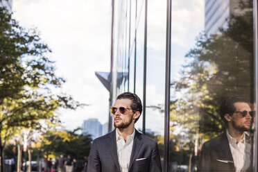 Geschäftsmann mit Sonnenbrille, die sich auf einem Glasgebäude in der Stadt spiegelt - CAVF47816