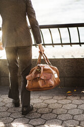 Low section of businessman carrying bag while standing at railing against sky - CAVF47829