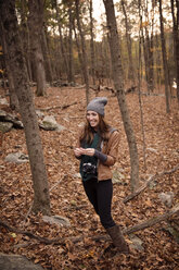 Lächelnde Frau mit Kamera inmitten von Bäumen im Wald im Winter - CAVF47880