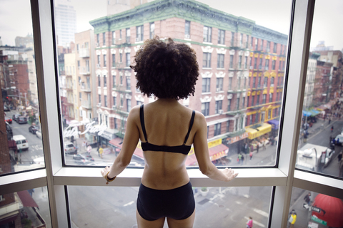 Rückansicht einer halbbekleideten Frau, die durch ein Fenster schaut, während sie in der Stadt steht, lizenzfreies Stockfoto
