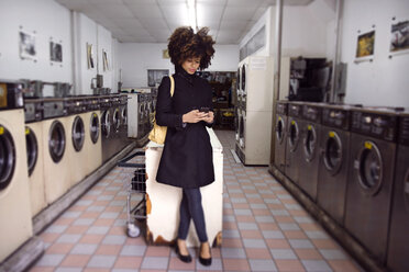 Frau in voller Länge beim Telefonieren im Waschsalon stehend - CAVF47924