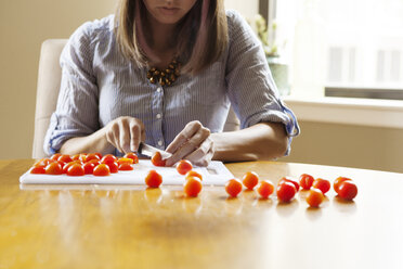 Mittelteil einer Frau, die Tomaten auf einem Schneidebrett an einem Holztisch schneidet - CAVF47932