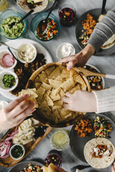 Draufsicht auf Freunde, die Nacho-Chips zu sich nehmen, während sie bei einem geselligen Beisammensein am Tisch essen - CAVF48118