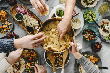 Cropped hand of friends taking nacho chips while having food at table - CAVF48119