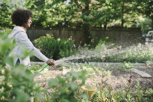 Side view of mature woman watering plants in garden - CAVF48137