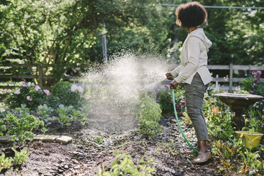 Side view of mature woman watering plants in yard - CAVF48138