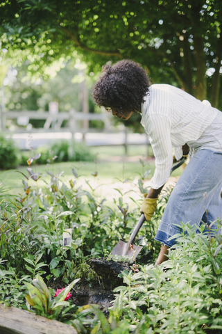 Frau gräbt Erde mit Schaufel im Garten, lizenzfreies Stockfoto