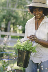 Glückliche reife Frau hält Topfpflanze im Garten - CAVF48154