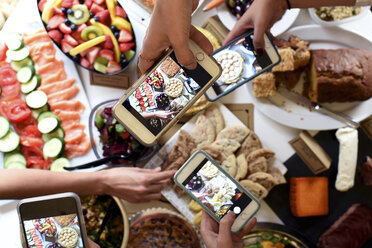 Ausgeschnittene Hände von Menschen, die mit ihren Smartphones auf einem Tisch am Buffet Essen fotografieren - CAVF48157