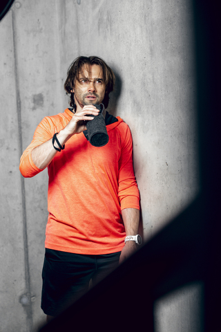 Athlete wearing standing at concrete wall drinking from flask stock photo