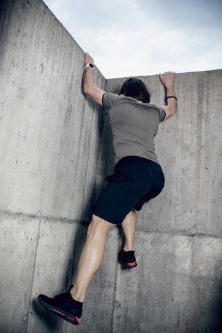 Athlete climbing up concrete wall outdoors stock photo