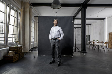 Portrait of mature businessman in front of black backdrop in loft - PDF01563