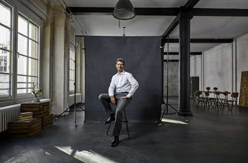 Portrait of mature businessman in front of black backdrop in loft - PDF01564