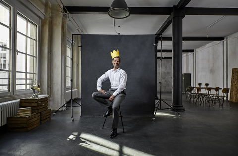 Portrait of mature businessman with crown in front of black backdrop in loft stock photo