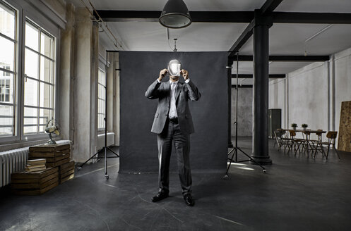 Mature businessman holding refecting mirror in front of black backdrop in loft - PDF01568