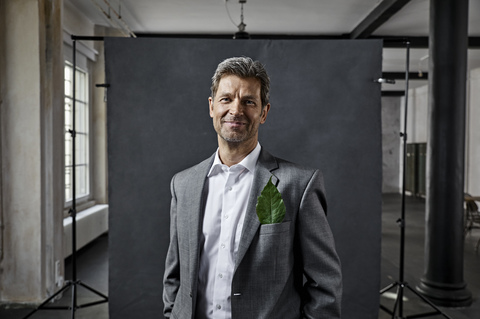 Portrait of mature businessman with leaf in pocket in front of black backdrop in loft stock photo