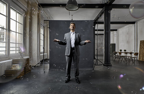 Mature businessman with bubbles standing in front of black backdrop in loft - PDF01570