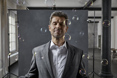Portrait of mature businessman with bubbles in front of black backdrop in loft - PDF01571