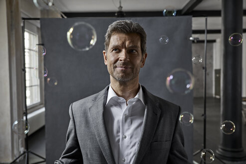 Portrait of mature businessman with bubbles in front of black backdrop in loft - PDF01572