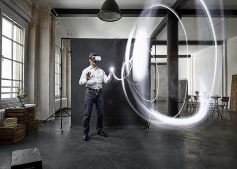 Älterer Mann mit VR-Brille Lichtmalerei vor schwarzem Hintergrund im Loft, lizenzfreies Stockfoto