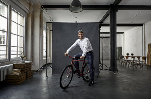 Porträt eines reifen Geschäftsmannes auf einem Fixie-Fahrrad vor einem schwarzen Hintergrund in einem Loft - PDF01575