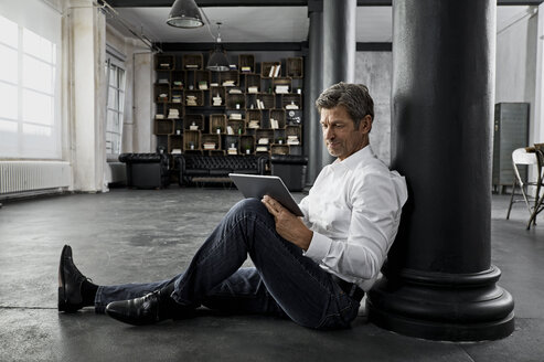 Mature man sitting on the floor using digital tablet in loft flat - PDF01583