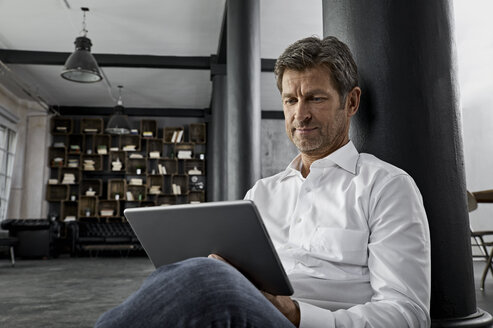 Mature man sitting on the floor using digital tablet in loft flat - PDF01584