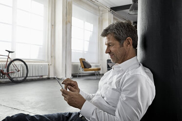 Älterer Mann sitzt auf dem Boden und benutzt sein Smartphone in einer Dachgeschosswohnung - PDF01586