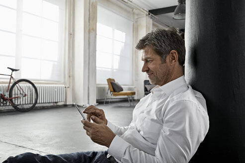 Mature man sitting on the floor using smartphone in loft flat - PDF01586