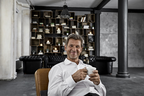 Portrait of mature man enjoying cup of coffee in loft stock photo