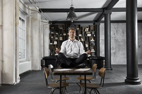 Portrait of mature businessman doing yoga on desk in loft office - PDF01615