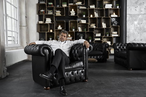 Porträt eines reifen Mannes, der in einem schwarzen Sessel in einem Loft sitzt, lizenzfreies Stockfoto