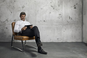 Älterer Mann mit digitalem Tablet vor einer Betonwand - PDF01619