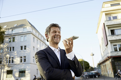 Lächelnder reifer Geschäftsmann mit Smartphone in der Stadt, lizenzfreies Stockfoto