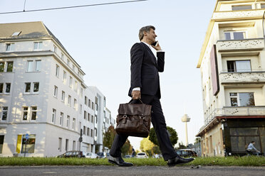 Älterer Geschäftsmann, der in der Stadt spazieren geht und sein Smartphone benutzt - PDF01624
