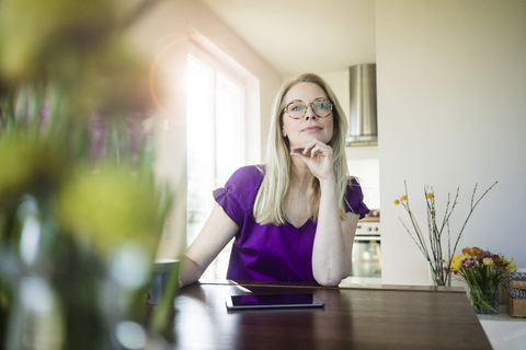 Porträt einer nachdenklichen Frau, die zu Hause am Tisch sitzt, lizenzfreies Stockfoto