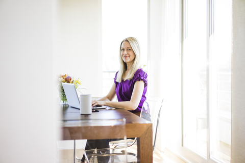 Porträt einer lächelnden Geschäftsfrau, die an einem Laptop arbeitet, lizenzfreies Stockfoto