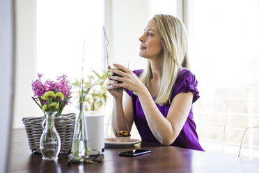 Reife Frau sitzt am Tisch und entspannt sich mit einem Glas Kaffee - MOEF01053