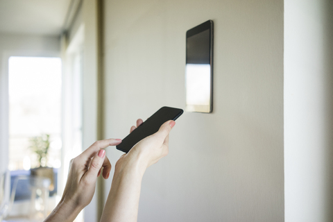 Die Hände einer Frau justieren ein digitales Tablet, das mit einem Smartphone an der Wand befestigt ist, lizenzfreies Stockfoto